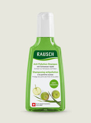 A bottle of Rausch Anti-Pollution Shampoo with green apple scent, featuring a translucent green bottle, white cap, and a white label with green apple graphics, set against a light beige background.