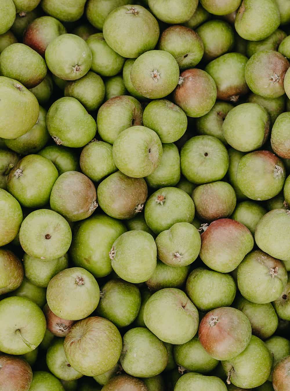 A close-up, top-down view of a dense pile of green apples with some showing light red blush tones.