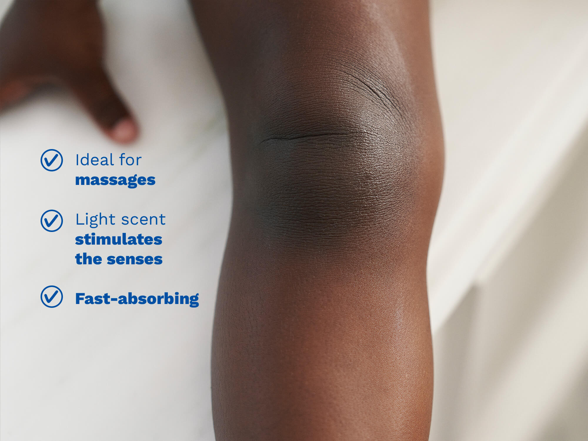 Close-up of a person's knee and upper thigh with blue text on the left listing benefits: 'Ideal for massages', 'Light scent stimulates the senses', and 'Fast-absorbing'.