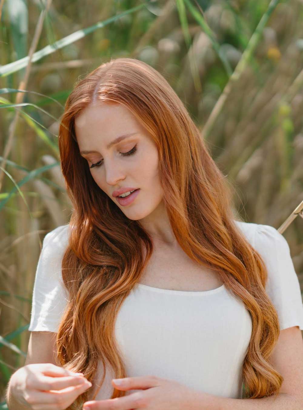 Woman with long red hair standing in a field of tall grass