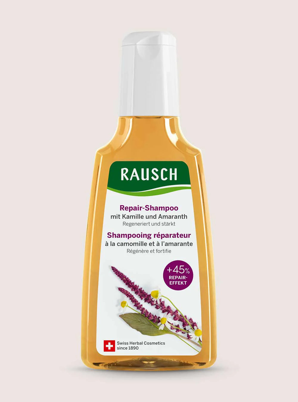 A bottle of Rausch Repair-Shampoo with Kamille und Amaranth on a light beige background. The bottle is made of translucent amber-colored plastic with a white cap and a white label featuring green and purple accents.