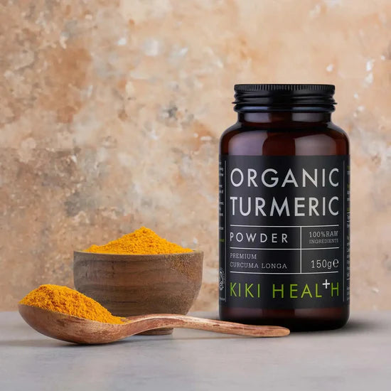 Kiki Health organic turmeric powder jar with a wooden spoon and bowl of turmeric on a beige background