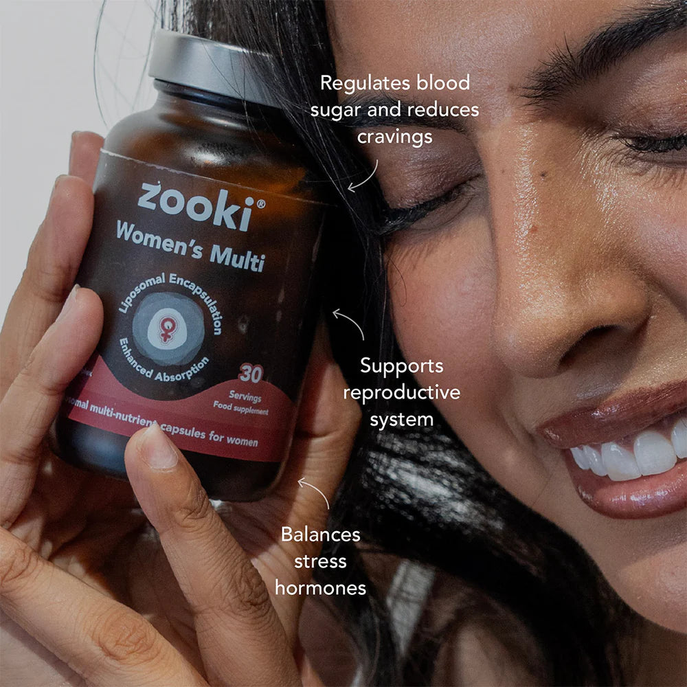 A woman holds a brown bottle of zooki Women's Multi supplement. The image features text callouts highlighting the product's benefits: 'Regulates blood sugar and reduces cravings', 'Supports reproductive system', and 'Balances stress hormones'.