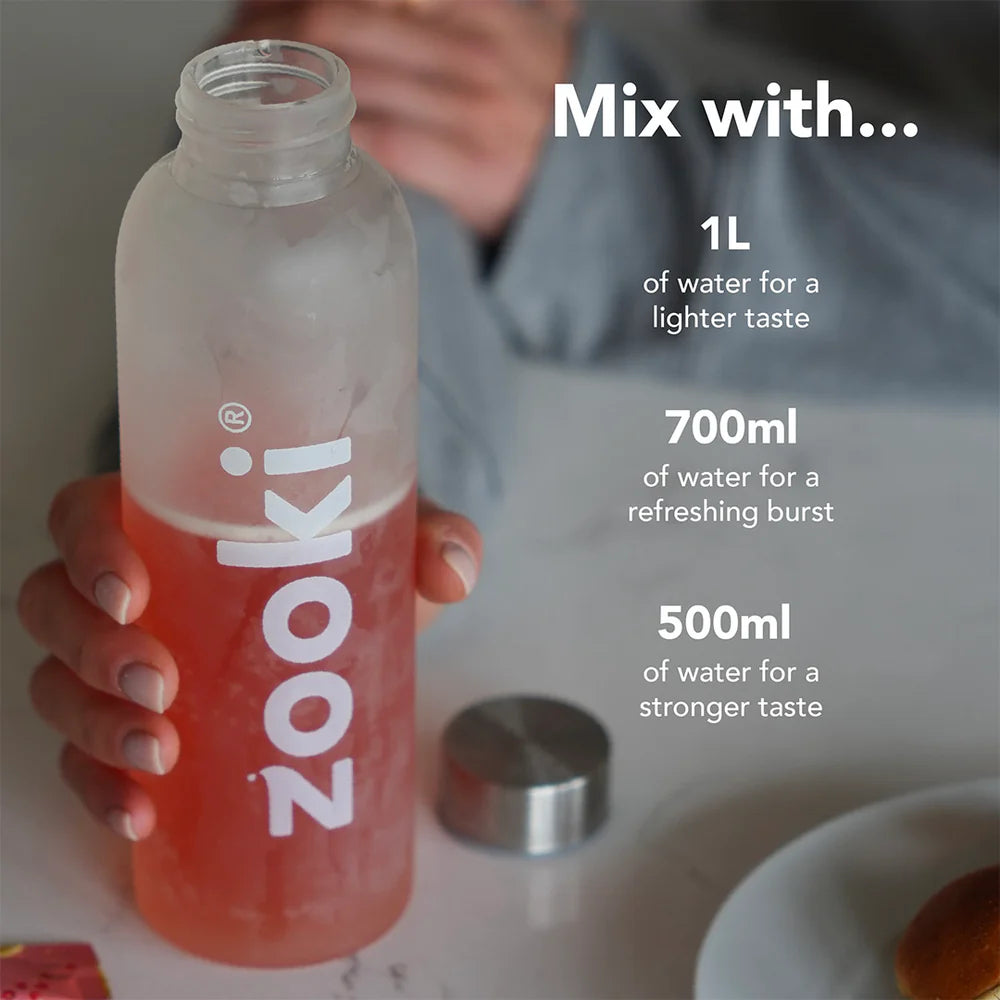 A frosted clear Nooki bottle with a silver cap, partially filled with a pink drink, held by a person in a kitchen setting. White text on the right explains mixing ratios with water: 1L for a lighter taste, 700ml for a refreshing burst, and 500ml for a stronger taste.